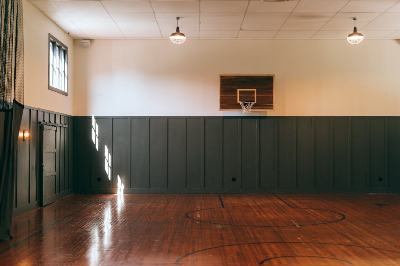 Empty indoor basketball court with wooden floor and minimal lighting.